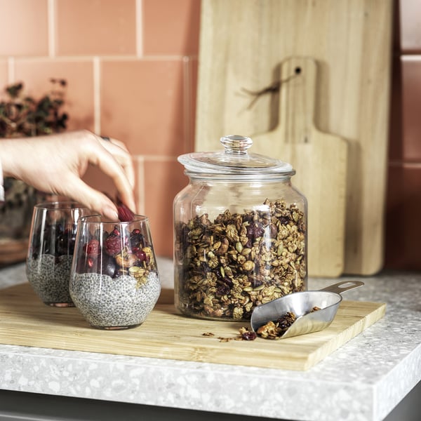 Pouring granola from jar onto board, with granola and fruit in glasses and a scoop.