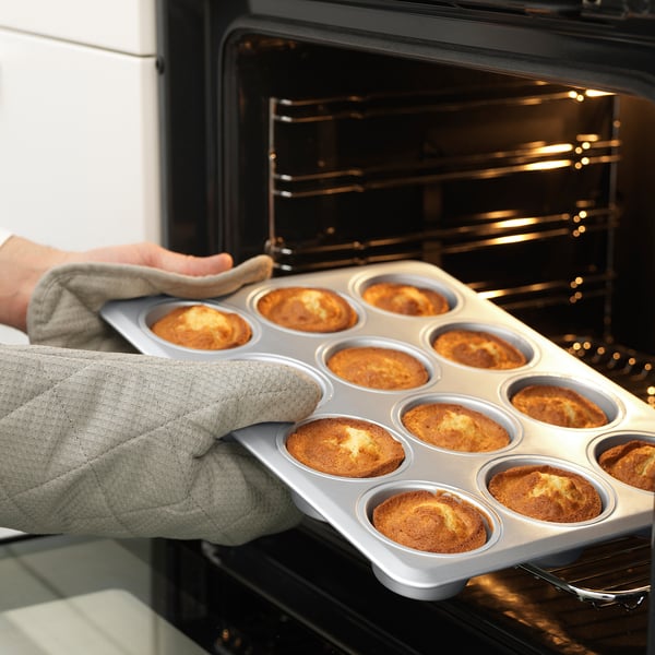 Person holding a muffin tin with baked muffins, using it to bake, showing durability and versatility.