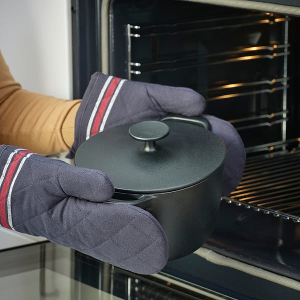 Person wearing oven mitts placing or removing a black pots/pans with lid into/from an oven.