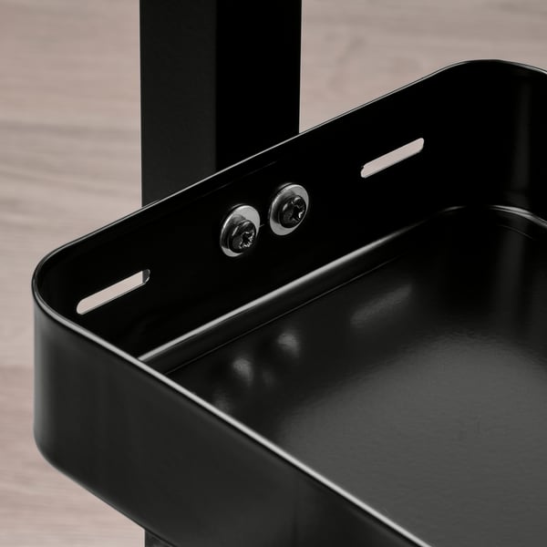 Black metal shelf unit with screws mounted on a table, featuring adjustable feet and scratch protection.