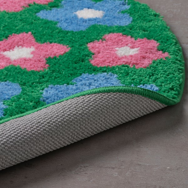 Bath mat with pink flowers, green leaves, and blue sky. Soft, thick pile for comfort. Non-slip grey underside.