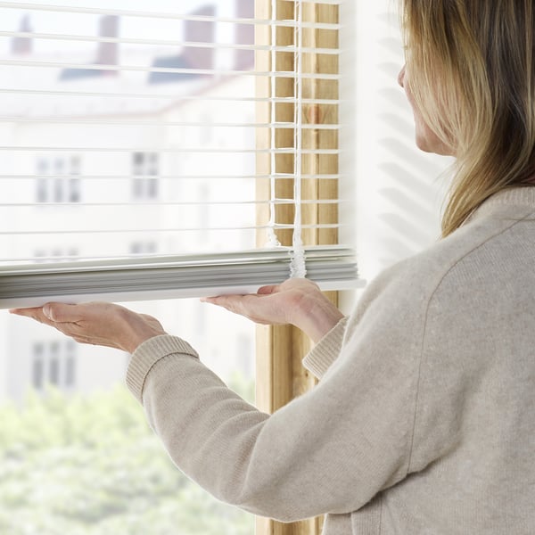 A person adjusts venetian blinds by pulling cords, controlling light and privacy.