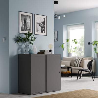 Grey VIHALS cabinet in modern living room with blue walls and black-and-white framed pictures, featuring sliding doors and decorative items on top.