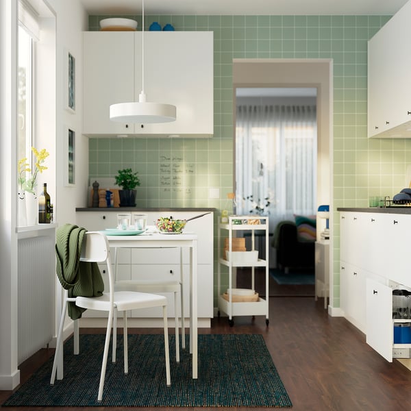 Modern kitchen with white chairs, wood floor, green walls, salad, wine, sweater.