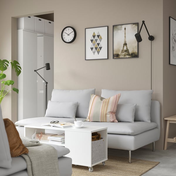 Modern living room with a white VIHALS sofa, featuring a mobile coffee table. Decorated with pastel pillows, black adjustable lamps, and wall art.