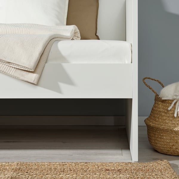 White daybed with mattress, folded blanket, and basket under open shelf against light blue wall.