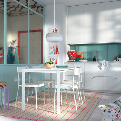 Bright kitchen with white VIHALS table and chairs. Large windows, blue accents, wooden bowls, and colourful rug.