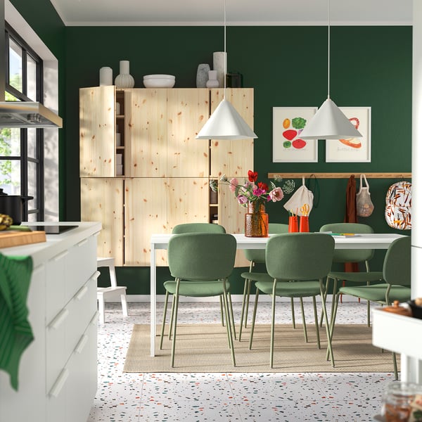 Modern kitchen with green walls, light wood cabinets, green dining chairs, pendant lamps, colourful rug, terrazzo floor, wall artwork.