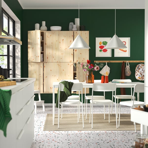 Modern kitchen with green walls, wooden cabinet, white dining set, terrazzo floor, and decorative items.