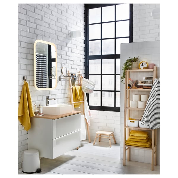 Modern bathroom with brick walls, a window, and a ladder shelf. Yellow towels and decor.