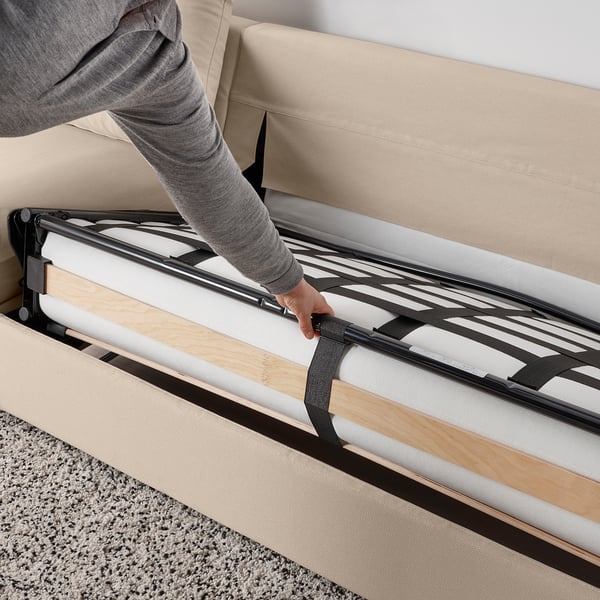 Person adjusting sofa-bed mechanism. Easy-convert bed with thick mattress and metal slats ensures comfortable sleep.
