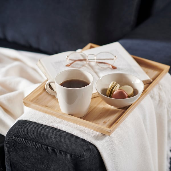 Wooden tray on couch, holding coffee mug, macarons, and glasses.