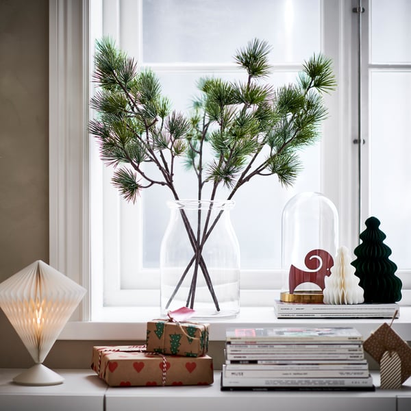 VINTERFINT, green pine stem in clear vase, decorated window sill, surrounded by books, gifts, and festive decor.