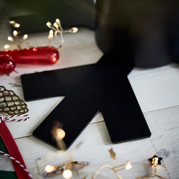 Black metal christmas tree holder, stable & adjustable, on white wooden table with festive decorations.