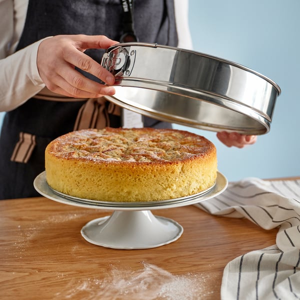 A person removes a pan from a baked cake on a stand, showcasing the springforms easy release feature.