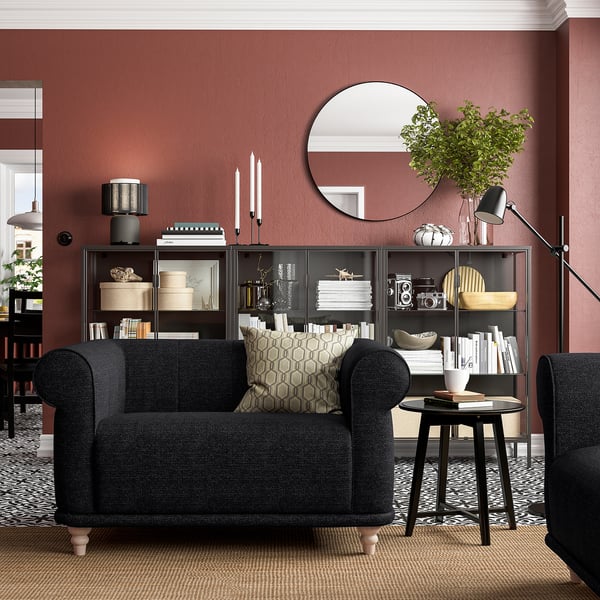 Dark grey VISKAFORS armchair, round mirror, bookshelf, red wall, cosy living room setup.