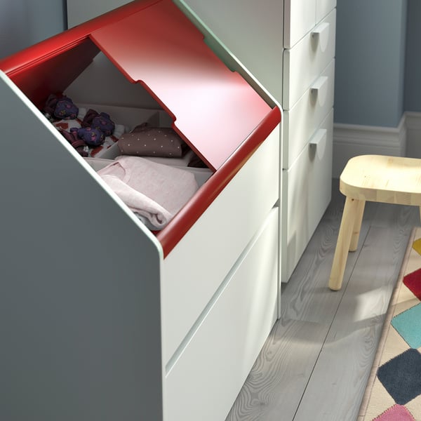 Open red-lid toy box with blankets and stuffed animals, grey drawer unit, and a small wooden stool.