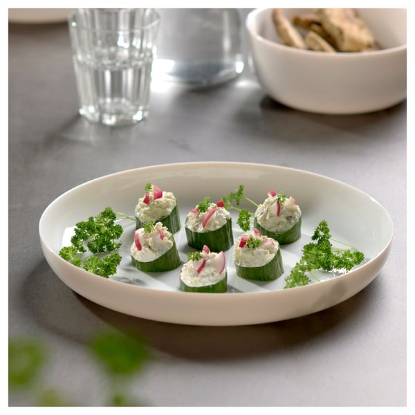 White plate with cucumber bites and garnish. Glass and parsley visible.