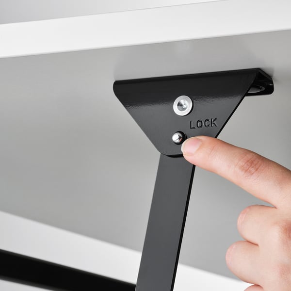 Hand pressing button labelled lock on an adjustable VITTERYD coffee table, ensuring tabletop stability.