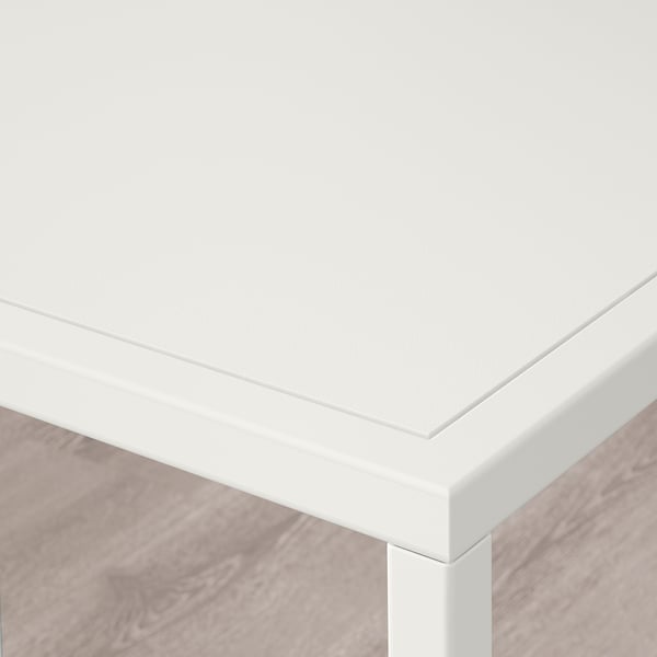 Corner of modern white table with glass top, showing sleek design and sturdy base.