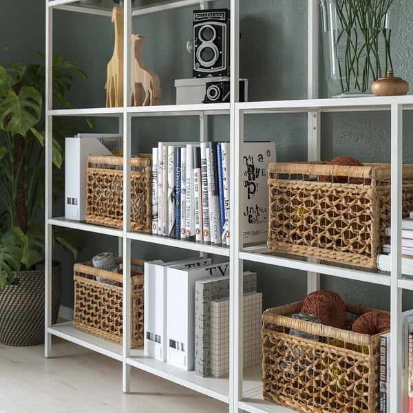 White metal shelf unit with glass, displaying books, woven baskets, and decorative items.