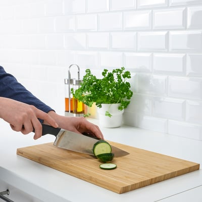 Person slicing cucumber on wooden cutting board with sharp, sturdy VÖRDA knife.