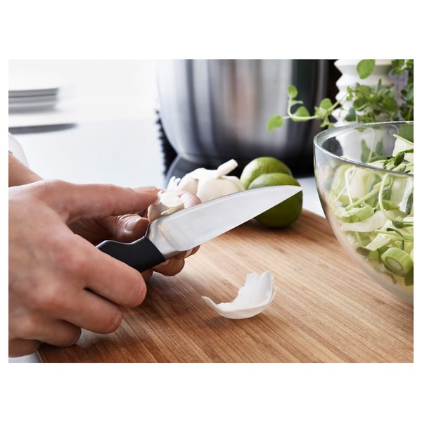 Person peels garlic cloves on cutting board using small, sharp paring knife with ergonomic handle near bowl of prepared vegetables.