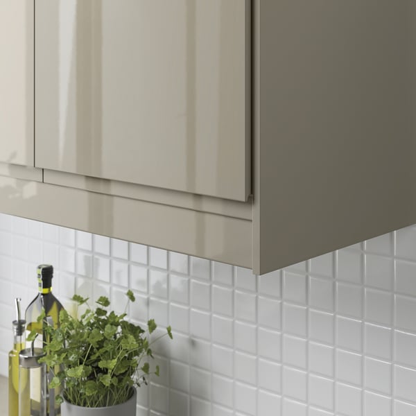 Modern kitchen cabinet with sleek, reflective edge trim covering under-cabinet lighting and cords. Fresh herbs in front.