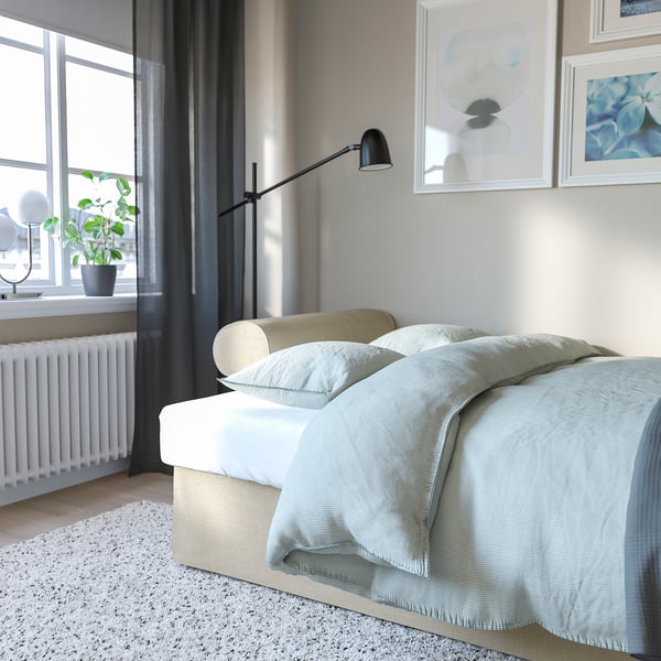 Bedroom with VRETSTORP sofa-bed, light blue cover, under black lamp, next to window with plant.