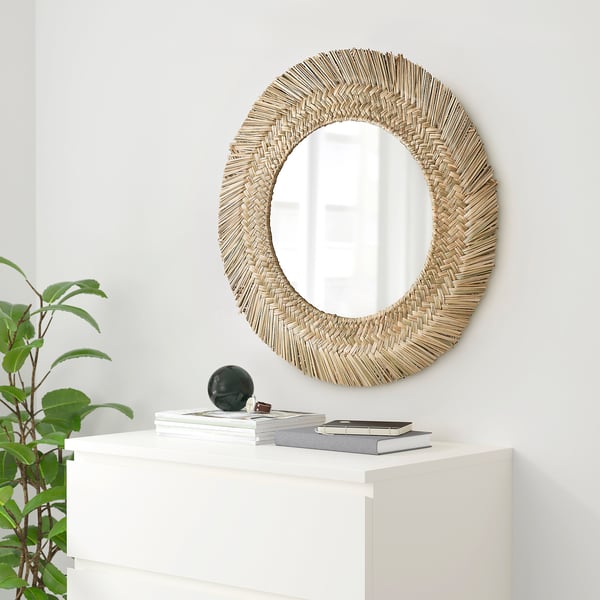 Round woven frame mirror above white cabinet, with green plant.