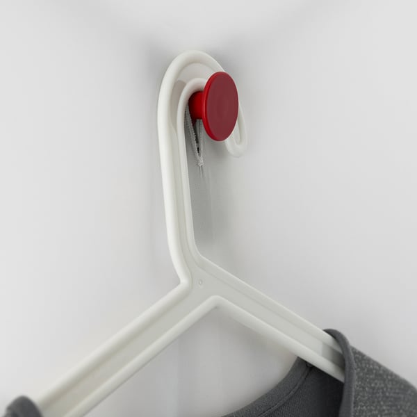 A white clothes hanger with a red button is attached to a grey wall. Part of the VUKU wardrobe system.