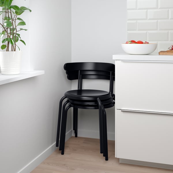 Stacked black chairs near white cabinet with bowl of fruit. Ideal for space-saving.