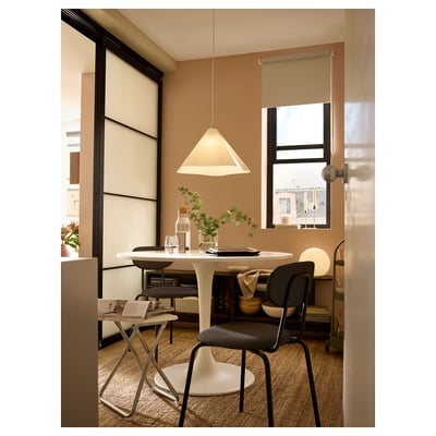 Modern dining area with round table, ZEBRASÄV lamp, vases, glasses, plants, and bright window.