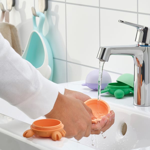 Laps peseb käsi segisti all, kasutades erksavärvilisi vannimänguasju.