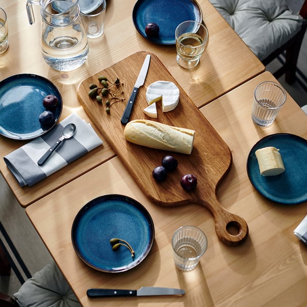 Puidust vorstilaud juustude, leiva, puuviljade ja siniste taldrikute, klaaside ja salvrätikutega.