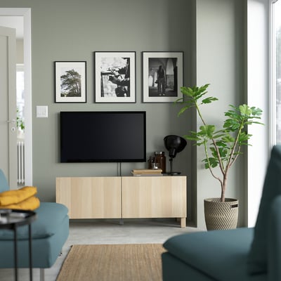 Kaasaegne elutuba, kus on BESTÅ helepuidust televiisor, salveirohelised seinad, kunst, taim, sinakasroheline diivan ja panipaik.