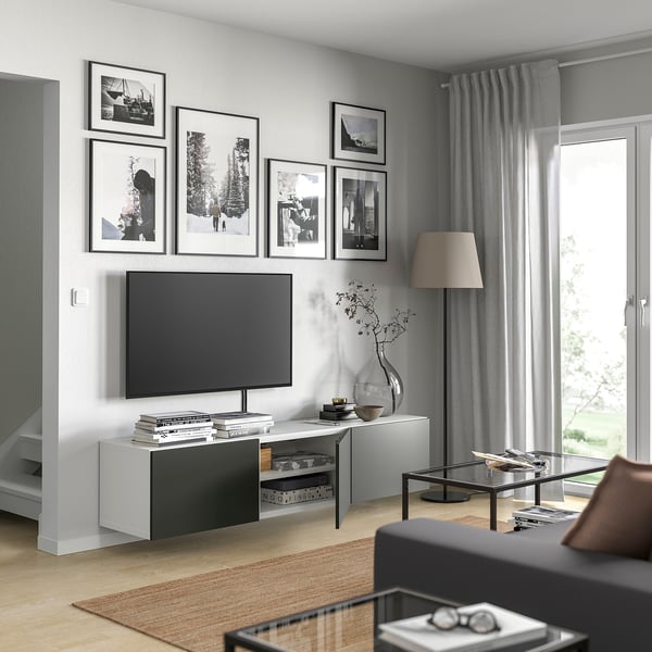 Kaasaegne elutuba valge televiisoriga BESTÅ televiisoriga. Lameekraaniga televiisor, raamitud fotod, hallid kardinad, beež lamp, klaaslaud raamatutega, puitpõrand.