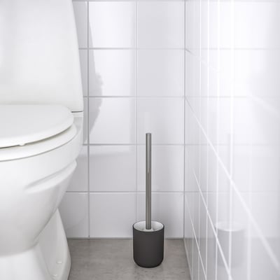 Must hõbedase käepidemega tualettharja hoidja valge WC-poti kõrval plaaditud põrandal.