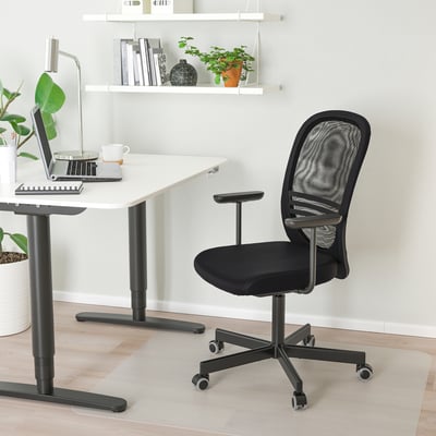 Ergonoomiline must kontoritool võrkseljatoega, käetugedega, kompaktse laua all sülearvuti ja kohviga.