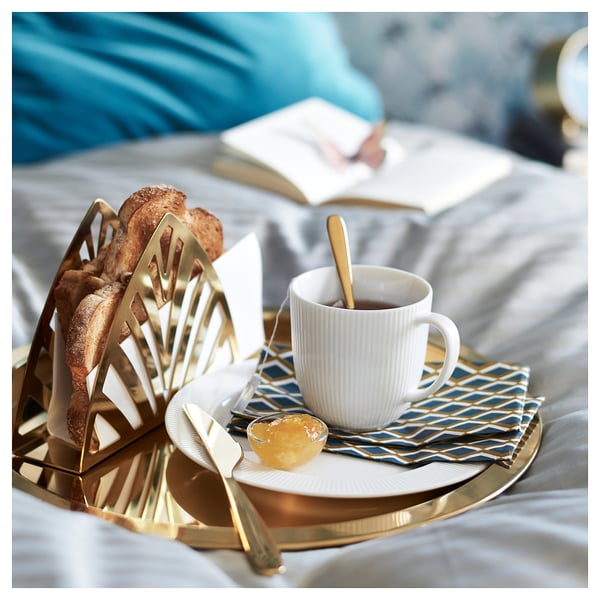 Messingist kandik leiva, kohvi, moosi, noa, lusikaga sinisel salvrätikul, valge voodi.