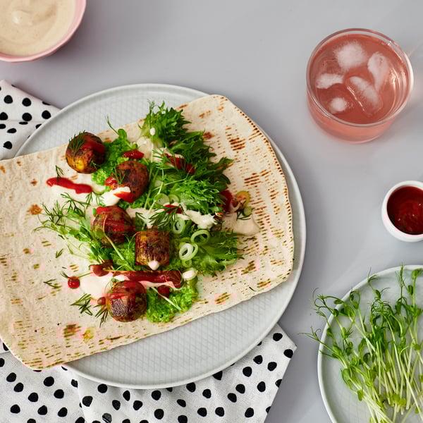 Lameleiva wrap rohelise salati, kastme ja lihaga valgel taldrikul koos joogiga.