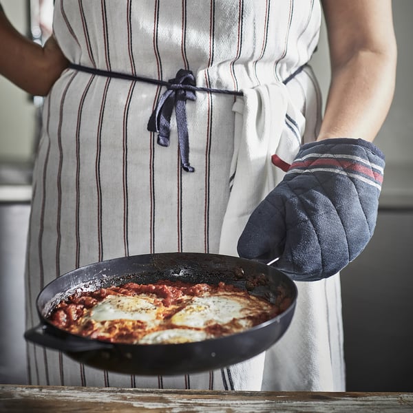 Halli triibulise põllega inimene hoiab musta ahjukinda abil shakshuka panni.