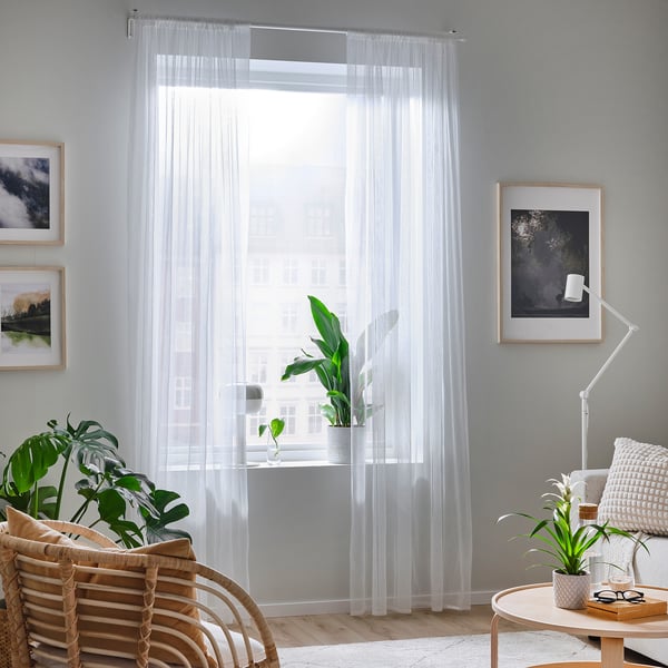 Minimalistlik elutuba HILDRUN valgete läbipaistvate kardinate, puitmööbli ja taimedega. Valgus filtreerib läbi, luues rahuliku õhkkonna.