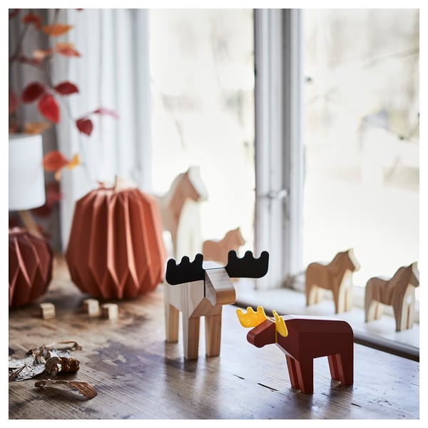 HÖSTAGILLE põdra dekoor. Väike puust põder, pruun kollaste sarvedega, seisab suurema oranži kõrvitsa ja puuhobuste läheduses.