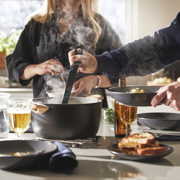 Naine küpsetab stiilsel mittenakkuva kattega pannil. Auruava ja mugav käepide on nähtavad.