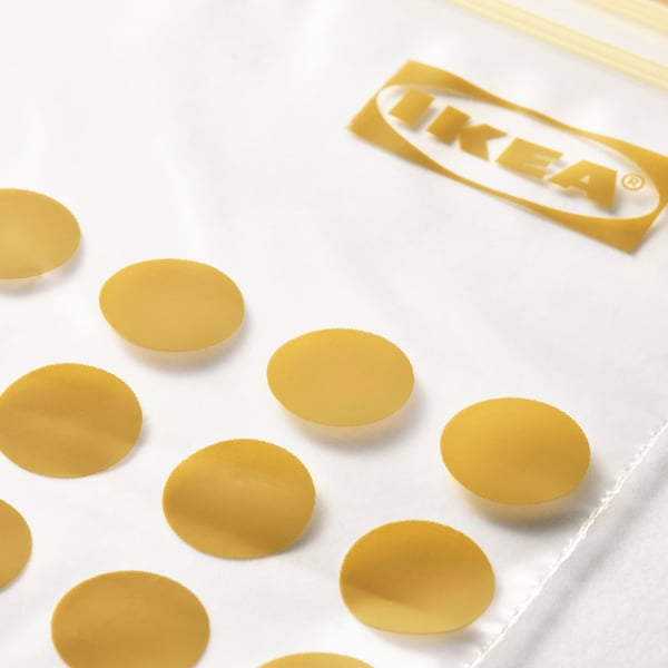 Mitu kuldset värvi ümmargust ikea ISTAD tihendit, mis on hajutatud valgele pinnale, taustal on näha ikea kaubamärgi silt.