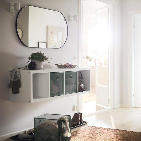 Valge võrksahtlitega KALLAX riiul, suure ovaalse peegli all, heleda ukseava lähedal.