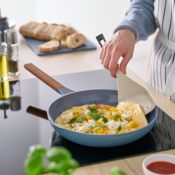 Inimene pöörab toitu sinisel pannil KNORRHANE spaatliga ümber. Spaatli lai tera ja kaldus käepide aitavad ümber pöörata ja serveerida.