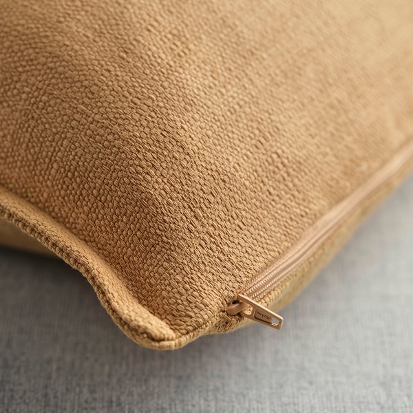 Lähivõte beežist mati tekstuuri ja kuldse tõmblukuga padjakattest.