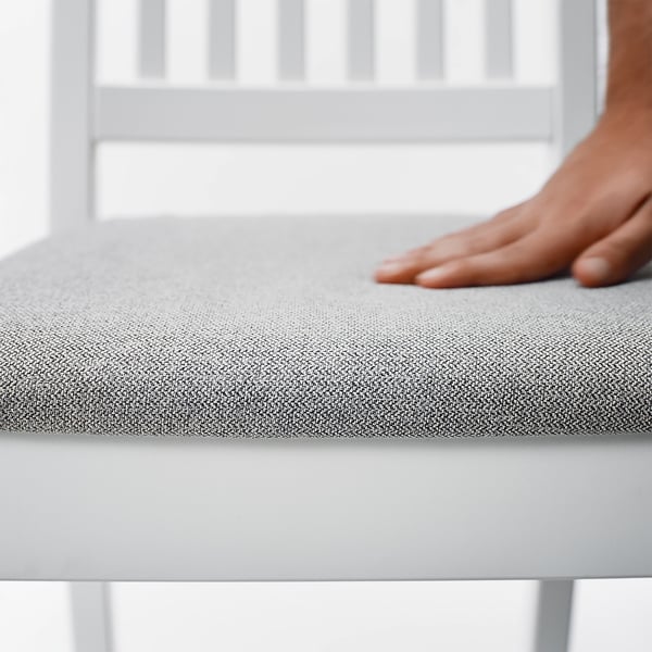 Inimese käsi, mis toetub moodsa tooli pehmele hallile polsterdatud istmele, rõhutades kanga mugavust ja kvaliteeti.